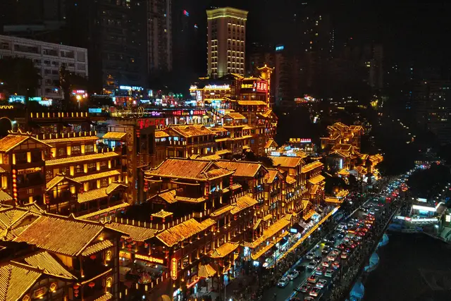 Hongyadong's tiered stilted buildings glowing gold at night above a busy riverside road in Chongqing