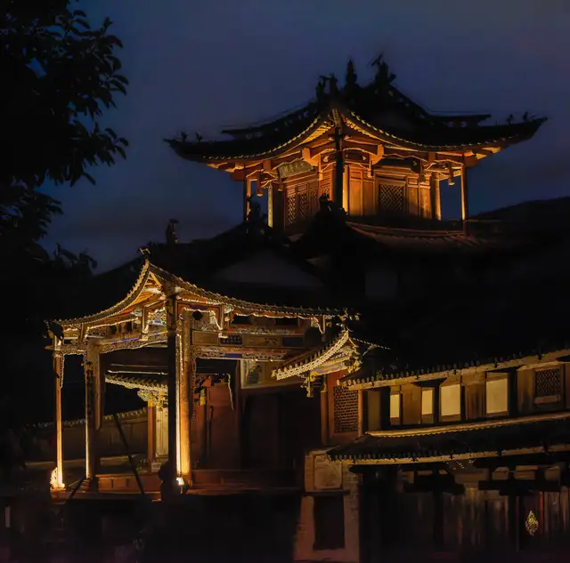 The old theatre stage on Sideng Square in Shaxi lit with warm lamps at night against a dark blue sky.