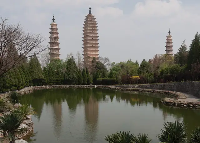 The Three Pagodas of Chongsheng Temple in Dali seen across a still pond that reflects the towers, framed by trees.