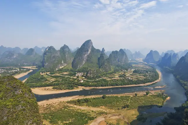 Green karst peaks rising above a bend of the Li River in Yangshuo County near Guilin, under a soft blue sky