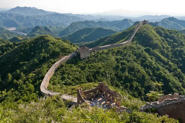 The Great Wall at Jinshanling snaking over green mountain ridges past its watchtowers, with layers of hazy hills behind.