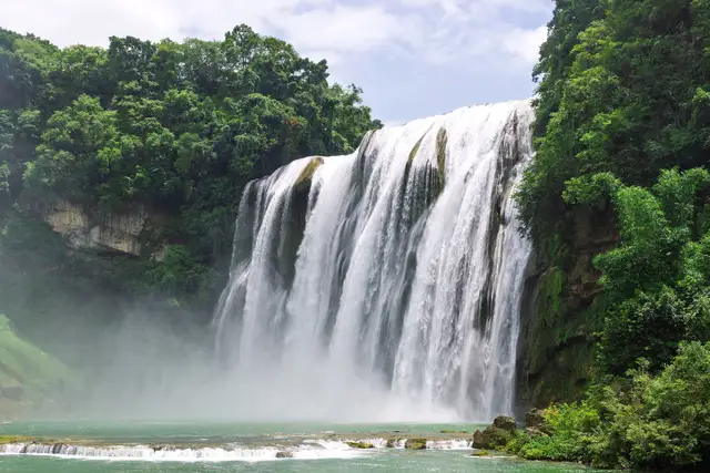 Huangguoshu Waterfall in full flow, white water plunging between green forested cliffs into a turquoise pool, Guizhou