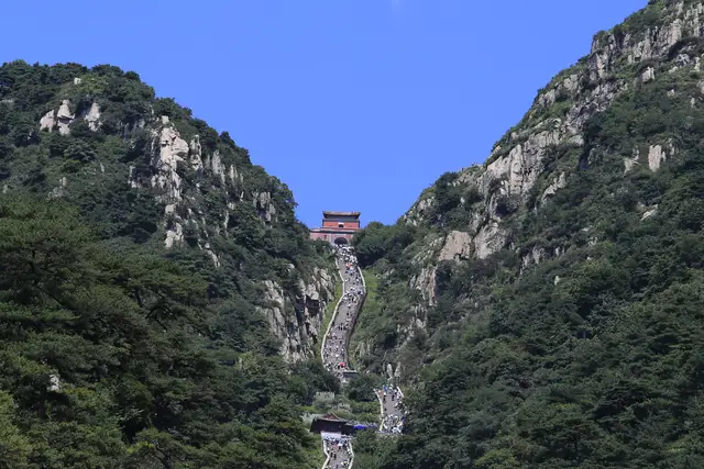 The Eighteen Bends stairway climbing between forested cliffs to the red South Gate to Heaven on Mount Tai, under a clear blue sky