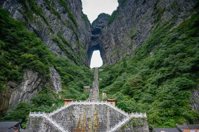 Tianmen Cave, the huge natural arch high in the cliffs of Tianmen Mountain in Zhangjiajie, with the long stairway climbing up to it through green forest.