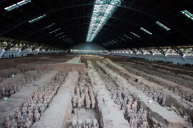 A wide view of Pit 1 of the Terracotta Army, with rows of clay warriors standing in long earthen trenches under the hall roof.