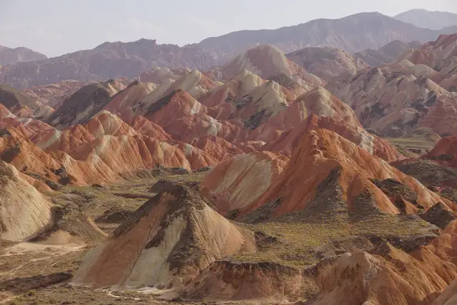 Layered red, orange and cream striped hills of the Zhangye Danxia landform in Gansu, stretching to distant mountains in late-afternoon light.